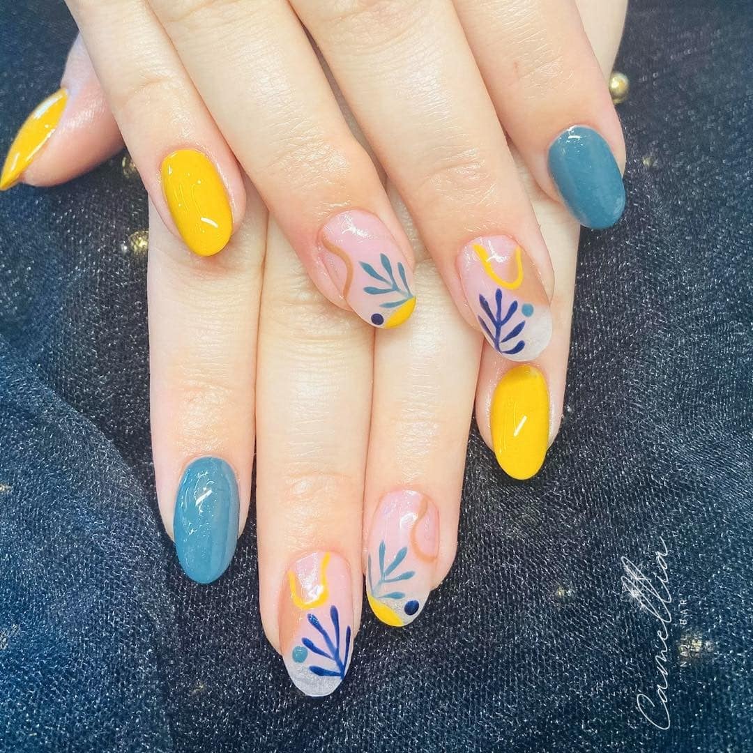 Freshly manicured hands with blue and yellow oval-shaped nails, featuring plant-like nail art